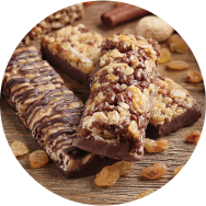 Three plant based chocolate protein bars on a wooden table with dried raisins sprinkled around them.